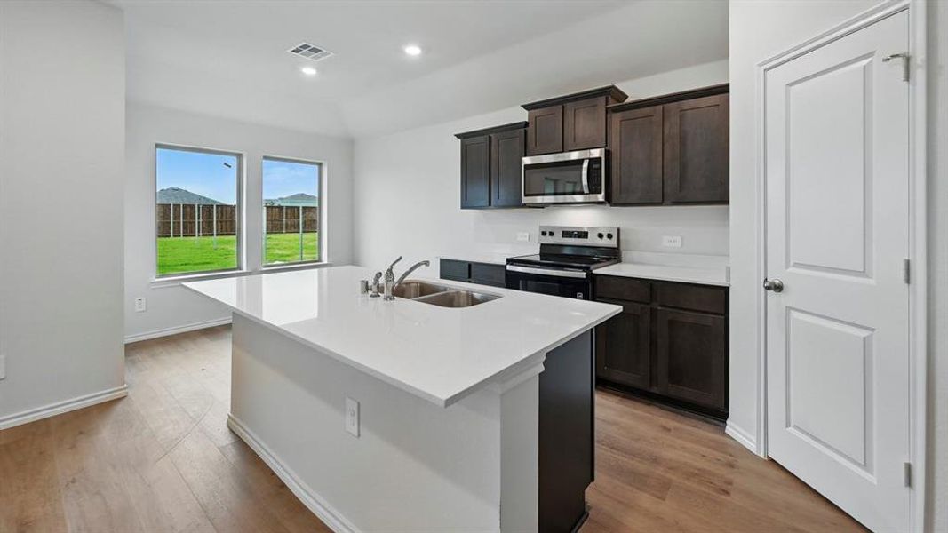 Kitchen with stainless steel appliances, an island with sink, recessed lighting, light wood-style flooring, and dark brown cabinetry