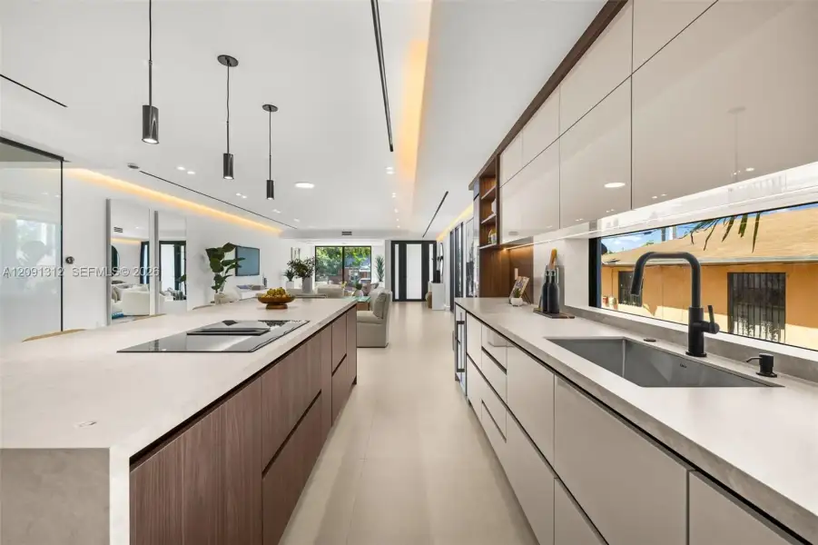 Modern kitchen featuring a spacious island with a built-in cooktop, high-gloss cabinetry, stone-finish countertops, matte black plumbing fixtures, and recessed accent lighting Modern kitchen featuring a spacious island with a built-in cooktop, high-gloss cabinetry, stone-finish countertops, matte black plumbing fixtures, and recessed accent lighting