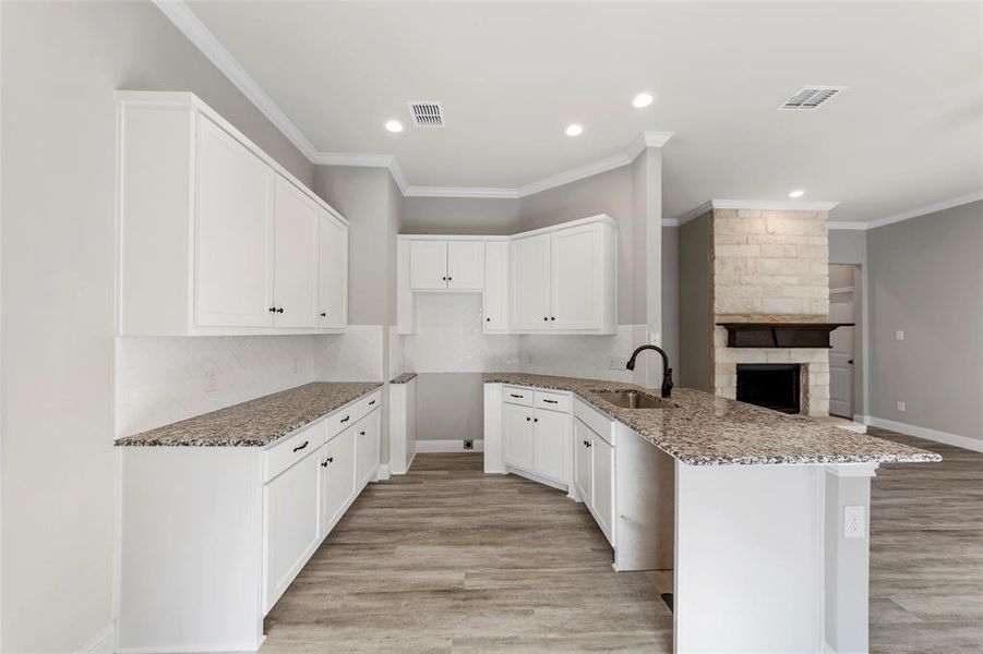 Kitchen with white cabinets, crown molding, sink, light wood-type flooring, and light stone counters