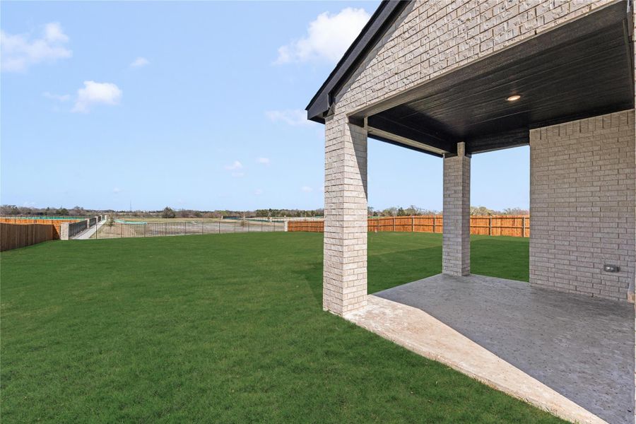 Covered brick patio overlooking large grassy backyard with wood privacy fence and open views beyond. Covered brick patio overlooking large grassy backyard with wood privacy fence and open views beyond.