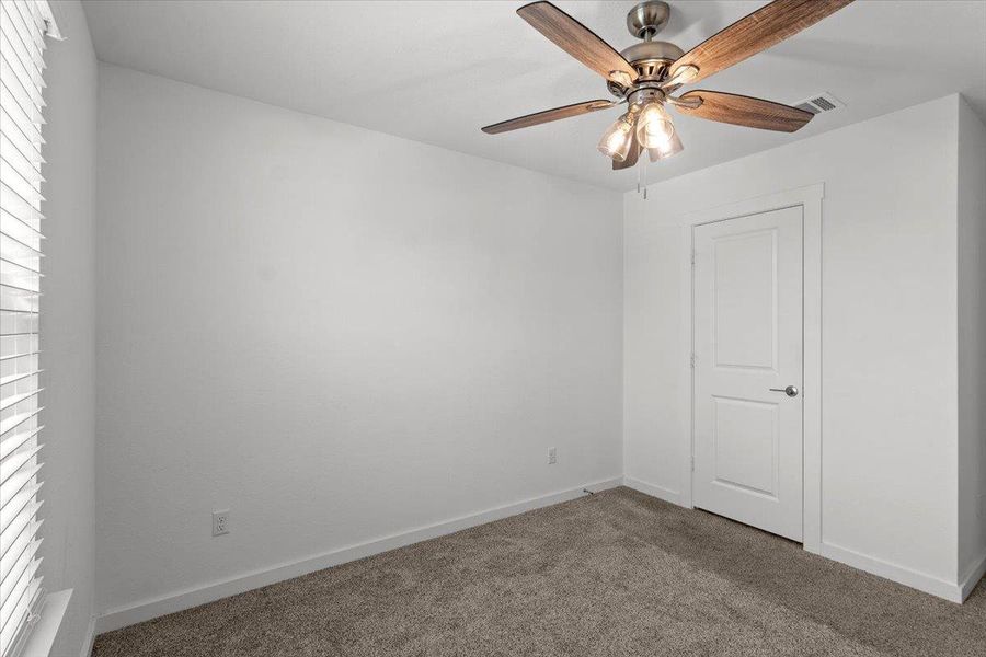 Well-lit room with plush carpeting and a versatile ceiling fan for comfort.