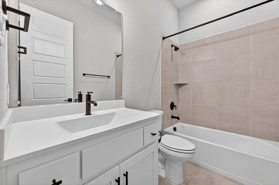 Bathroom featuring a white vanity with integrated sink, dark bronze fixtures, light-toned tile flooring, and a tiled shower-tub combination with a built-in niche Bathroom featuring a white vanity with integrated sink, dark bronze fixtures, light-toned tile flooring, and a tiled shower-tub combination with a built-in niche