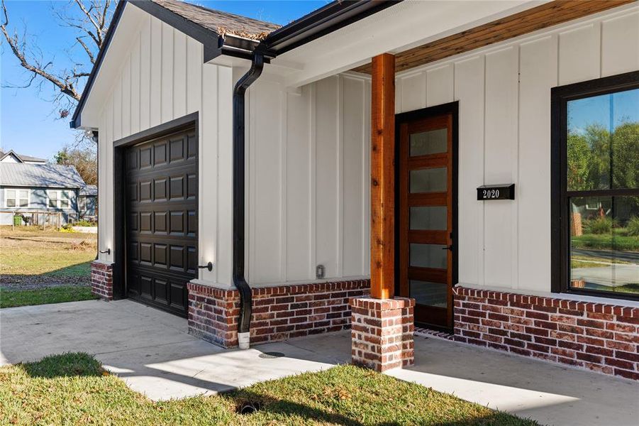 Doorway to property featuring a garage, board and batten siding, and brick siding