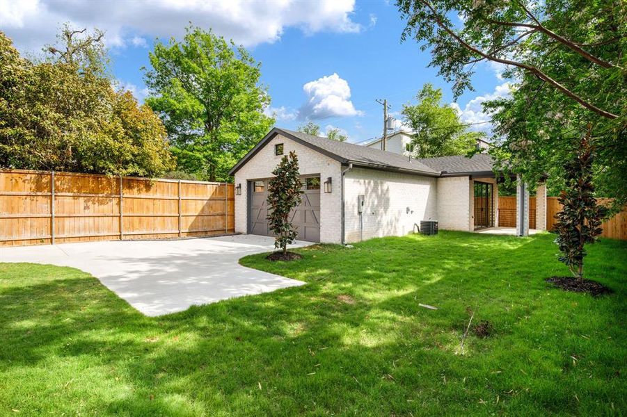 Spacious rear yard featuring a paved drive, a two-car garage with transom windows, and a privacy fence Spacious rear yard featuring a paved drive, a two-car garage with transom windows, and a privacy fence