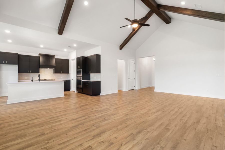 An open-concept great room and kitchen flow seamlessly under a vaulted ceiling with exposed beams and recessed lighting.