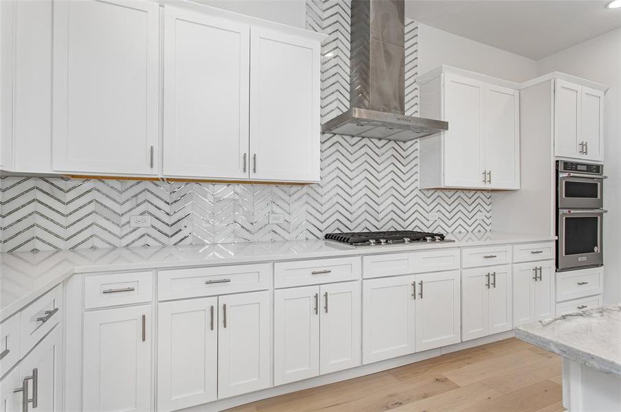 Kitchen featuring decorative backsplash, appliances with stainless steel finishes, white cabinetry, light hardwood / wood-style flooring, and wall chimney exhaust hood