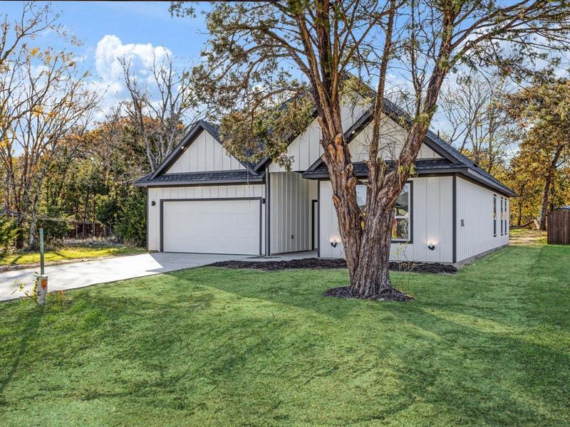 View of front facade featuring concrete driveway, a front yard, board and batten siding, and a garage