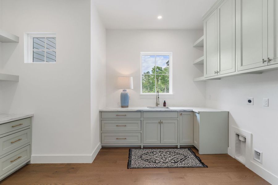 Spacious utility room with custom cabinetry, marble countertops, and a built-in sink under a window for natural light. Abundant drawer storage, upper cabinets, and open shelving provide plenty of organization space.