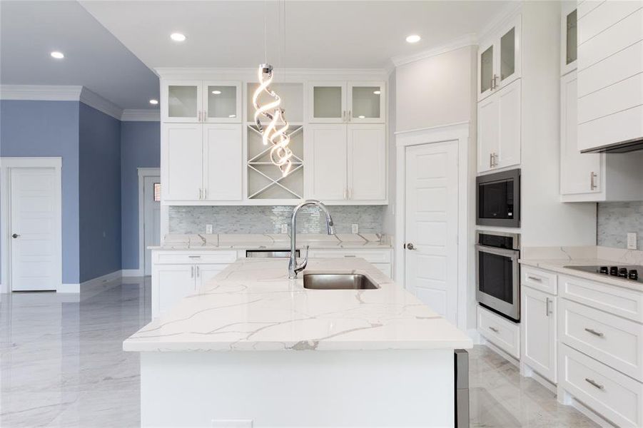 Kitchen featuring light stone counters, glass insert cabinets, ornamental molding, white cabinets, and decorative backsplash