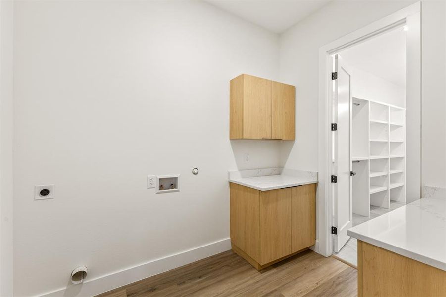 Laundry area featuring light wood-finish cabinetry, white countertops, and wood-finish flooring