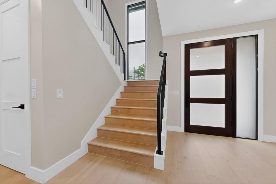 Natural light floods this inviting entryway, showcasing polished wood flooring and a sleek modern staircase.