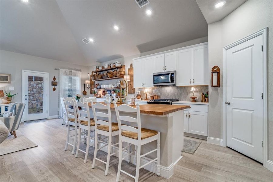 Kitchen featuring butcher block countertops, tasteful backsplash, white cabinets, an island with sink, and lofted ceiling Kitchen featuring butcher block countertops, tasteful backsplash, white cabinets, an island with sink, and lofted ceiling