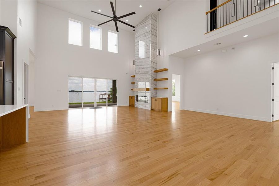 Unfurnished living room featuring light wood finished floors, a high ceiling, healthy amount of natural light, recessed lighting, and a fireplace