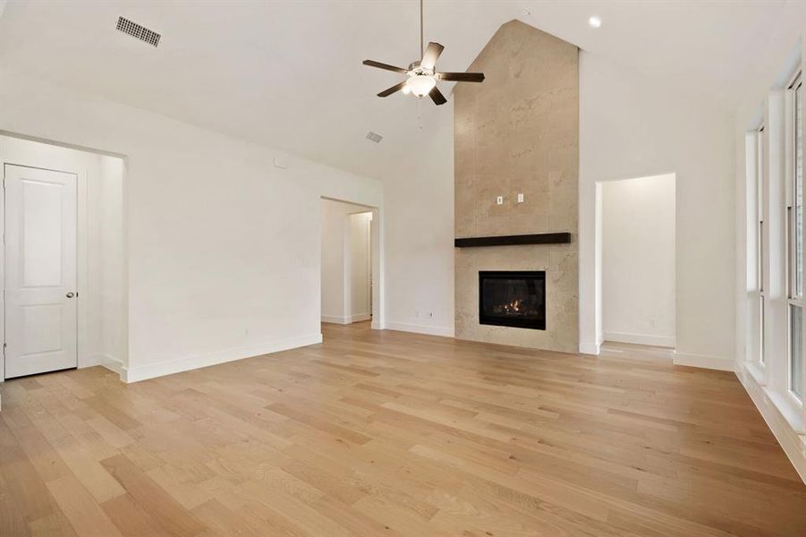 Unfurnished living room with a ceiling fan, lofted ceiling, light wood-style floors, and a tiled fireplace
