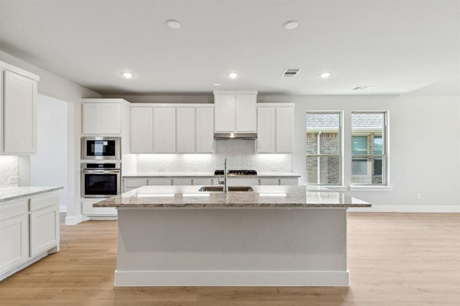 Kitchen with decorative backsplash, light stone countertops, appliances with stainless steel finishes, light wood finished floors, and recessed lighting Kitchen with decorative backsplash, light stone countertops, appliances with stainless steel finishes, light wood finished floors, and recessed lighting