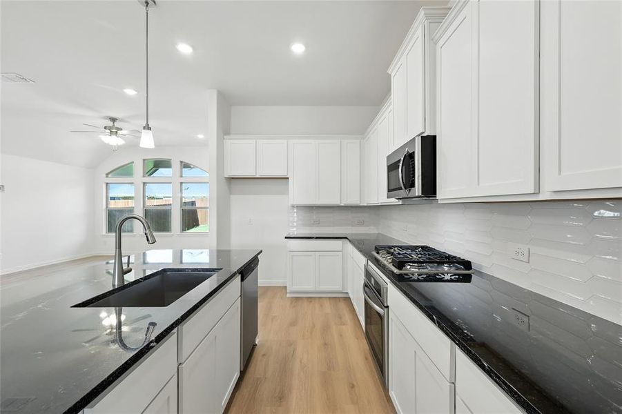 Kitchen featuring dark stone countertops, white cabinets, light wood-type flooring, and ceiling fan