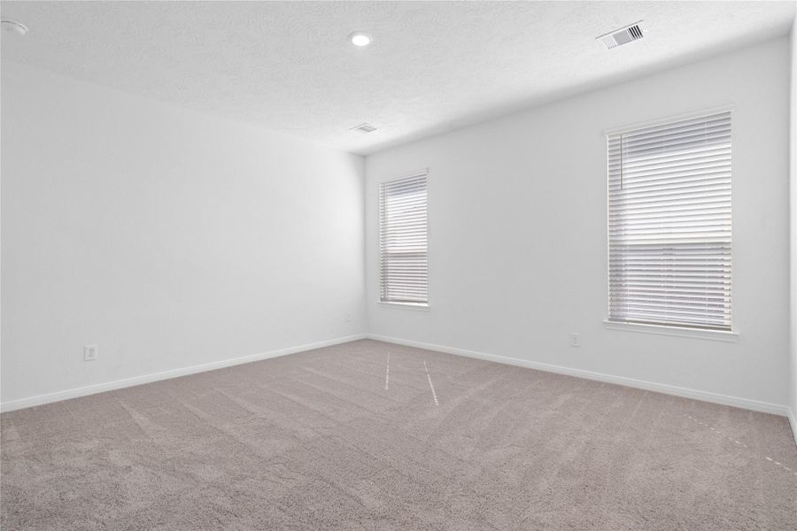 Enjoy a quiet escape in the primary bedroom, featuring large windows that fills the space with natural light, high ceilings, recessed lighting, plush carpet flooring, and a spacious ensuite bathroom.