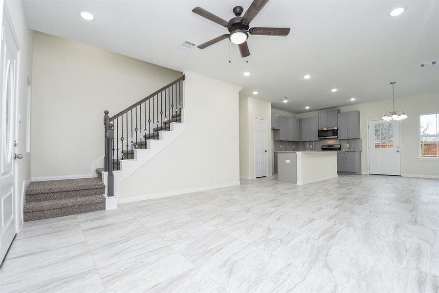 Modern, spacious interior with kitchen, staircase, tiled floor, and ceiling fan; neutral color scheme with natural light.