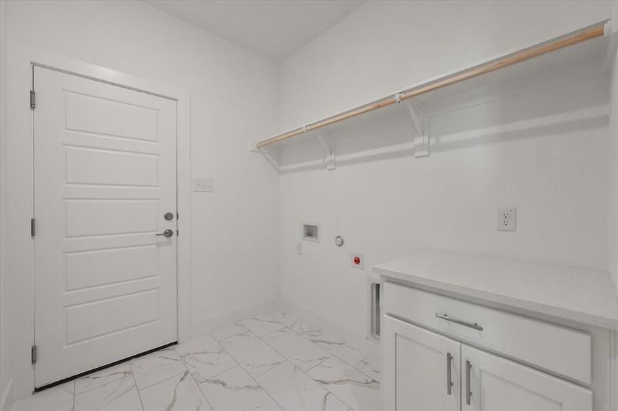 Laundry area / entry from garage featuring light marble finish flooring, hookup for washing machine & electric dryer, shelving with clothing rod and granite counter with cabinet space.