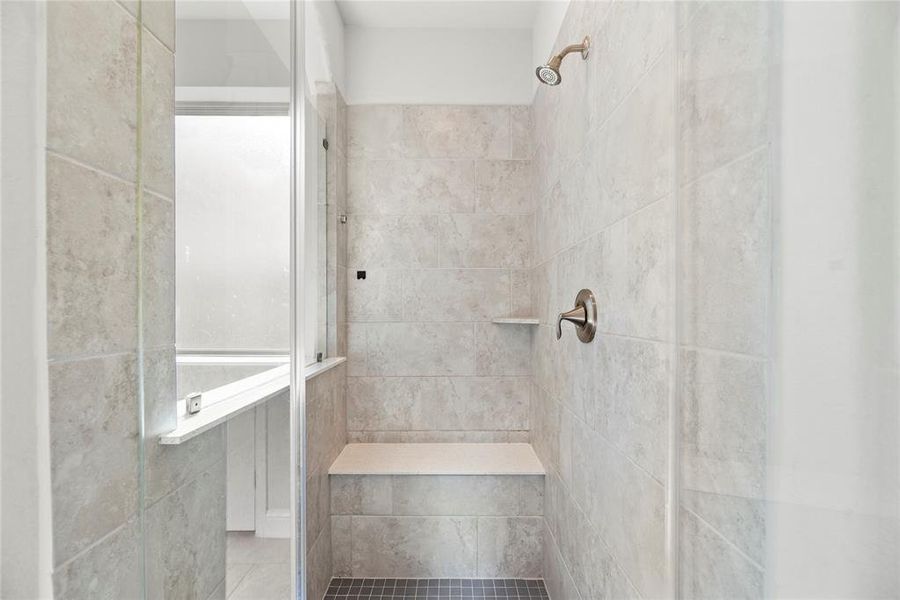 This is a walk-in shower with beige tile walls, a built-in bench, and glass enclosure. It features a frosted window for natural light and a dark floor for contrast.