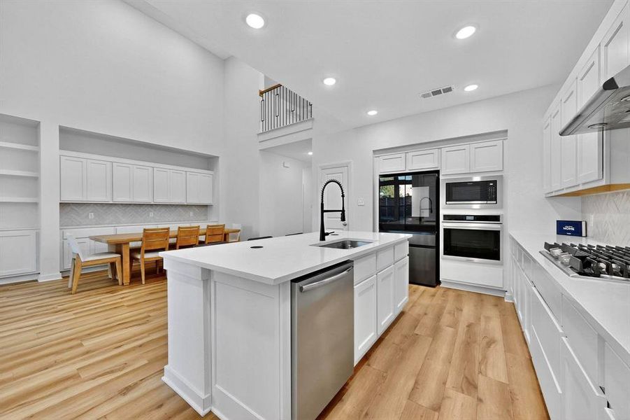 Kitchen featuring decorative backsplash, white cabinets, stainless steel appliances, light wood-type flooring, and recessed lighting Kitchen featuring decorative backsplash, white cabinets, stainless steel appliances, light wood-type flooring, and recessed lighting