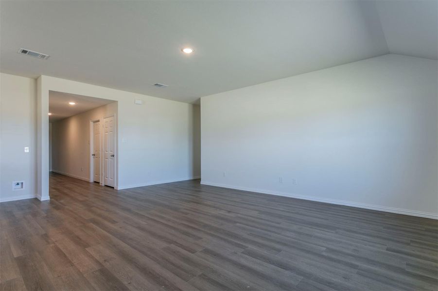 Empty room with recessed lighting, vaulted ceiling, visible vents, baseboards, and dark wood-style flooring
