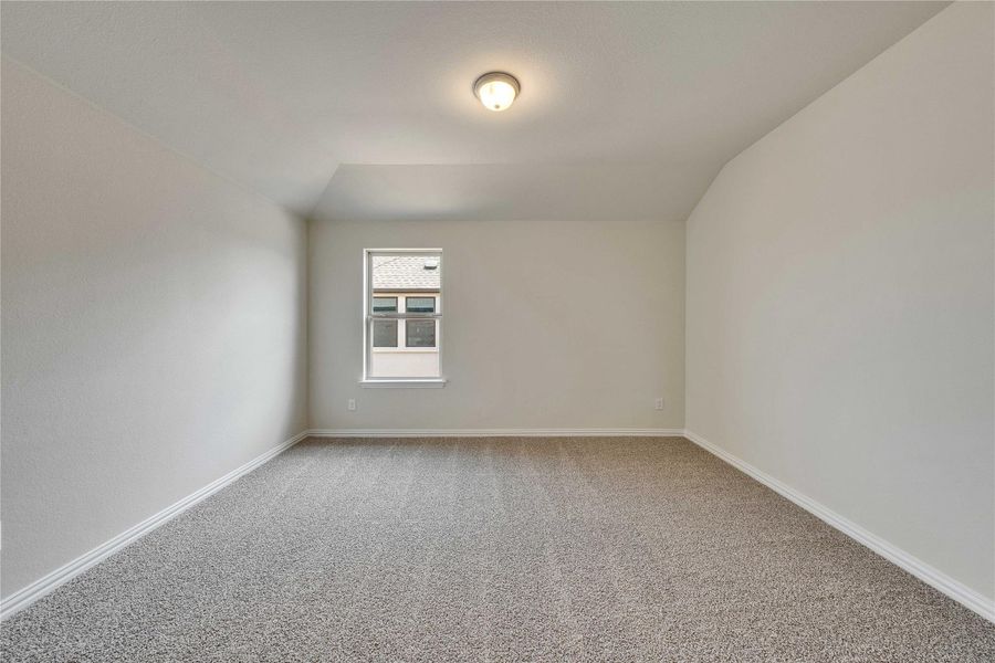 Carpeted empty room with lofted ceiling and baseboards Carpeted empty room with lofted ceiling and baseboards