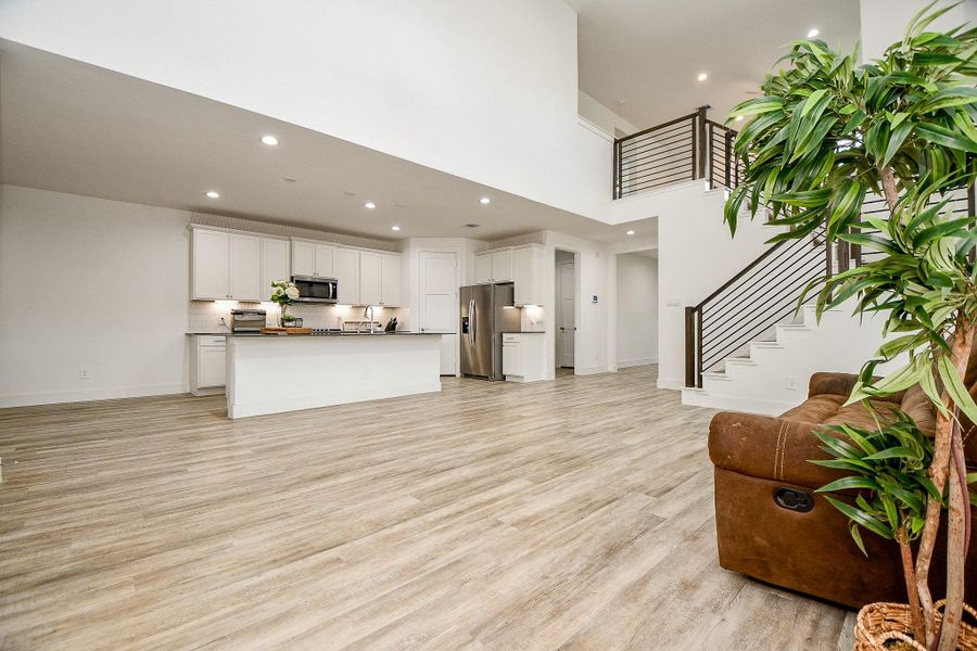 This spacious, modern open-concept living area features high ceilings, light hardwood floors, and a sleek kitchen with white cabinetry and stainless steel appliances. The room is bright, with a modern horizontal iron staircase and ample natural light, ideal for both relaxation and entertaining. This spacious, modern open-concept living area features high ceilings, light hardwood floors, and a sleek kitchen with white cabinetry and stainless steel appliances. The room is bright, with a modern horizontal iron staircase and ample natural light, ideal for both relaxation and entertaining.