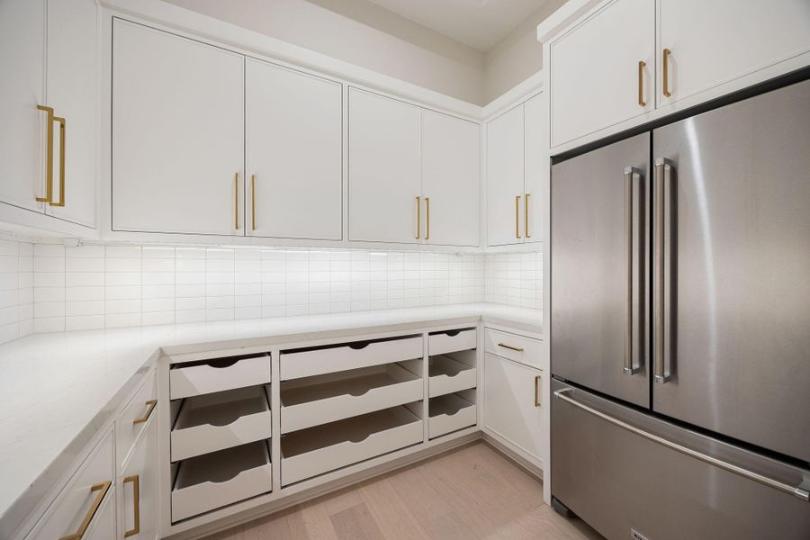 A well-appointed secondary prep kitchen designed for organization and efficiency. Clean white cabinetry, ample storage, and thoughtful layout create a highly functional workspace. The standout feature is the custom storage system with pull-out drawers, offering exceptional organization while maintaining a clean, streamlined aesthetic.