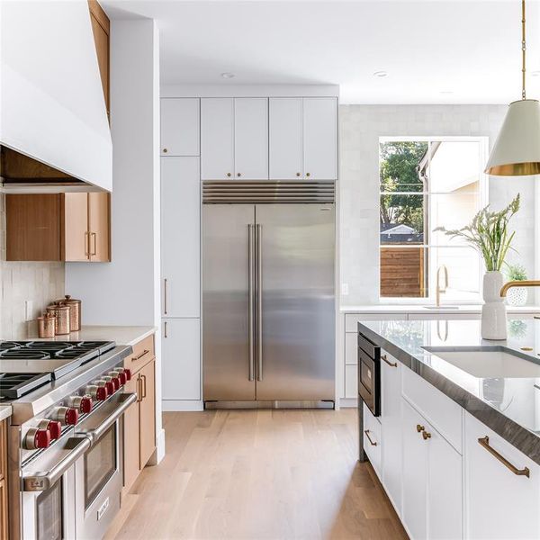 Kitchen with high quality appliances, custom range hood, white cabinetry, and light hardwood / wood-style flooring