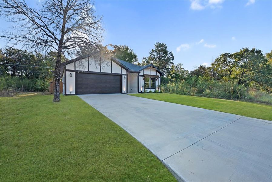 View of front of home featuring concrete driveway, a front lawn, and a garage