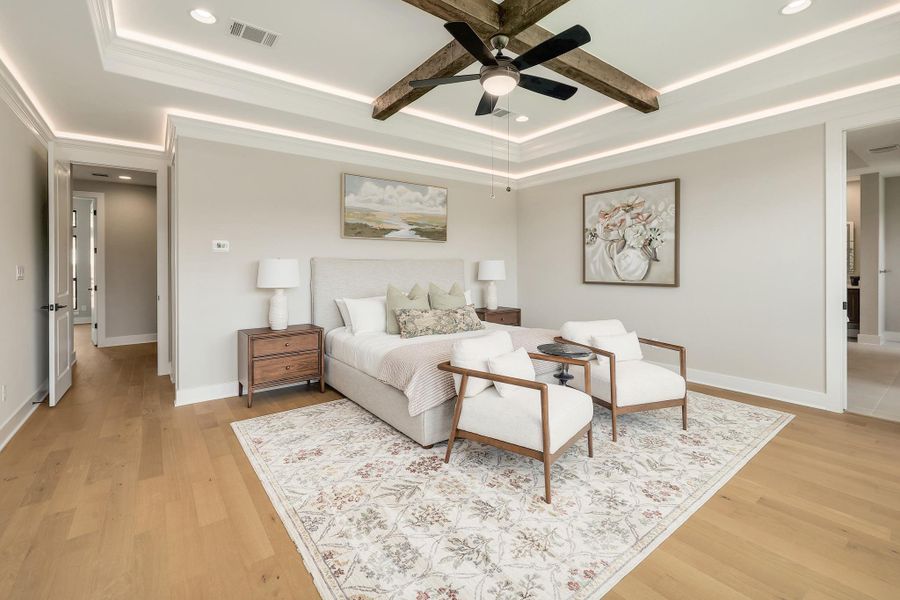 Tray ceiling, illuminated with integrated lighting and a rustic beam fan, anchors this serene primary bedroom retreat.