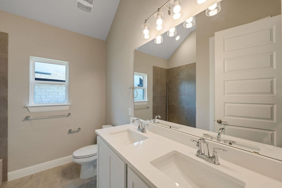 Full bathroom with vaulted ceiling, healthy amount of natural light, double vanity, and tiled shower