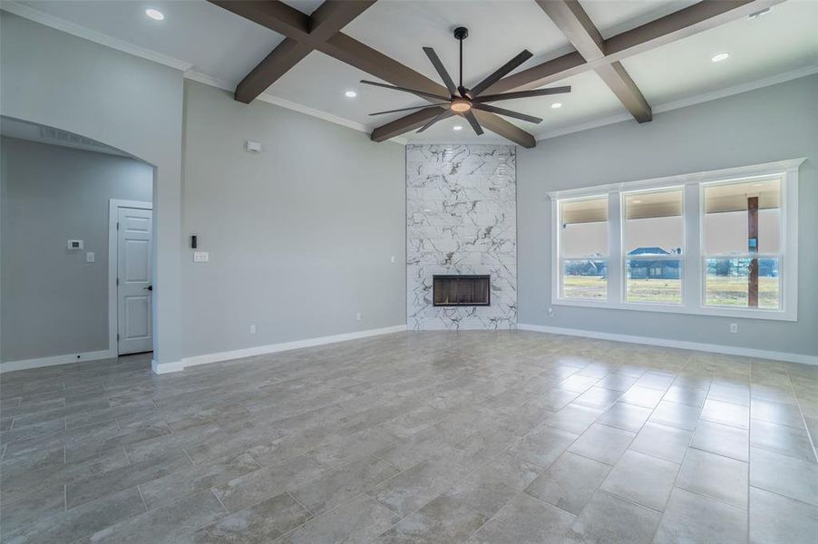 Unfurnished living room with a ceiling fan, coffered ceiling, arched walkways, a fireplace, and beam ceiling Unfurnished living room with a ceiling fan, coffered ceiling, arched walkways, a fireplace, and beam ceiling