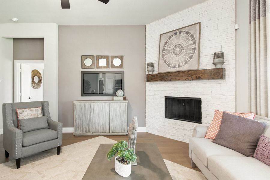 Living room with white stacked stone fireplace, wood mantel, gray sofa, and hardwood floors