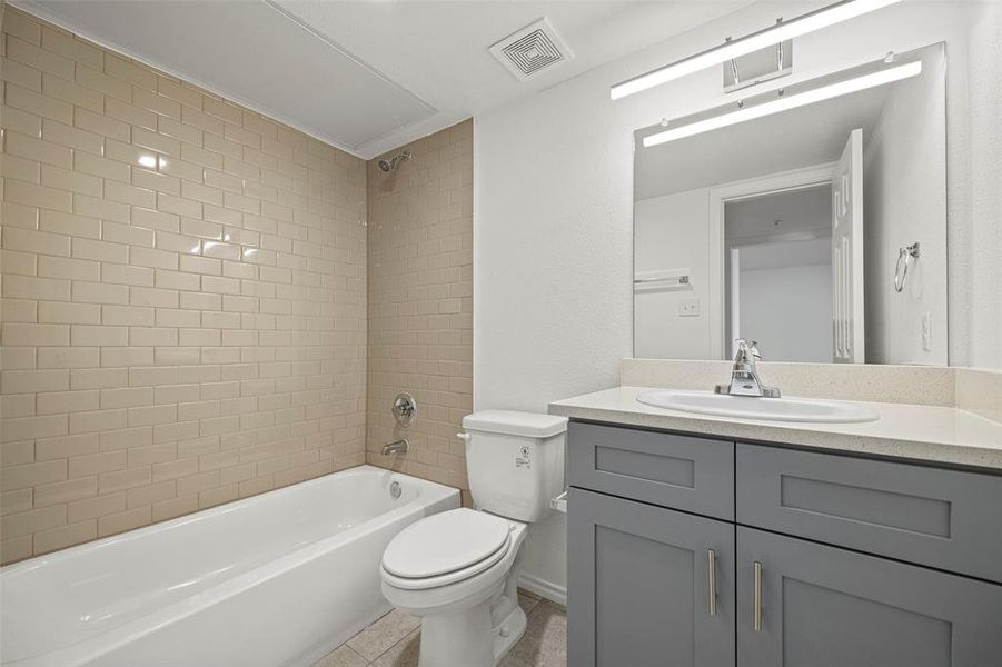 Full bathroom with tile patterned flooring, toilet, vanity, and tiled shower / bath