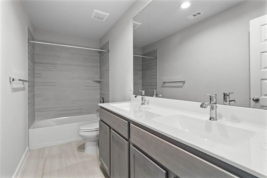 Secondary bath features tile flooring, bath/shower combo with tile surround, stained cabinets, dual vanities, beautiful light countertops, mirror, sleek fixtures and modern finishes.