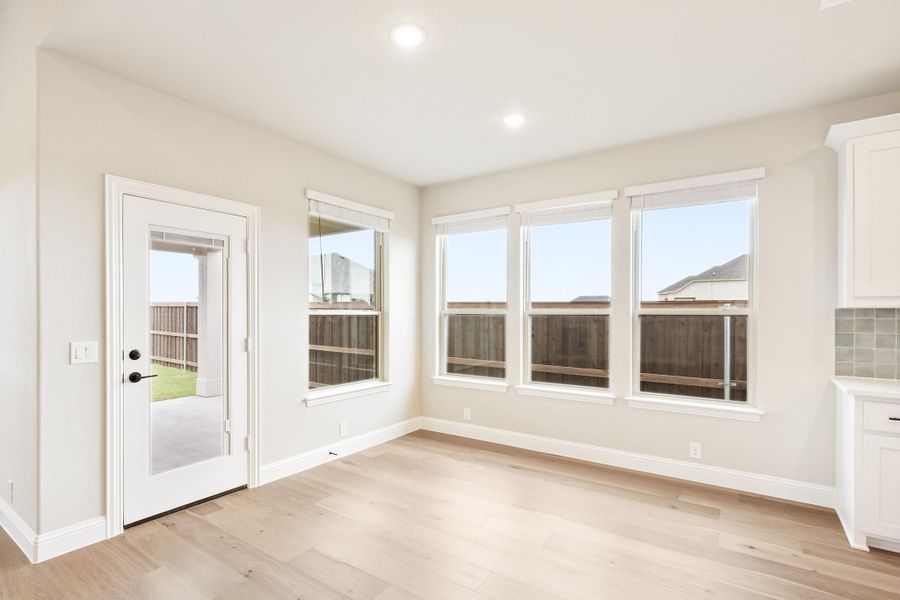 Bright dining nook with light wood floors, three windows, and glass back door leading to fenced yard