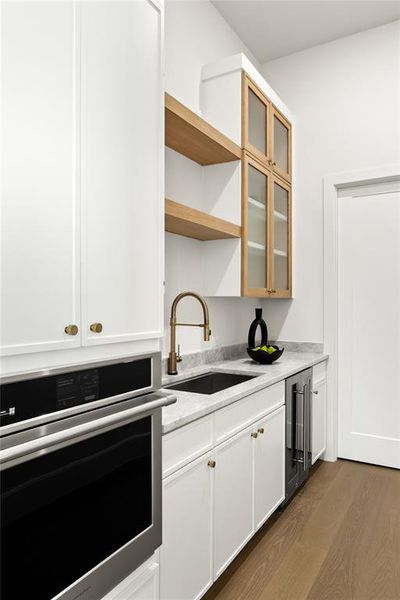 Modern kitchen area featuring a built-in stainless steel oven, white cabinetry with brass hardware, and light-colored countertops