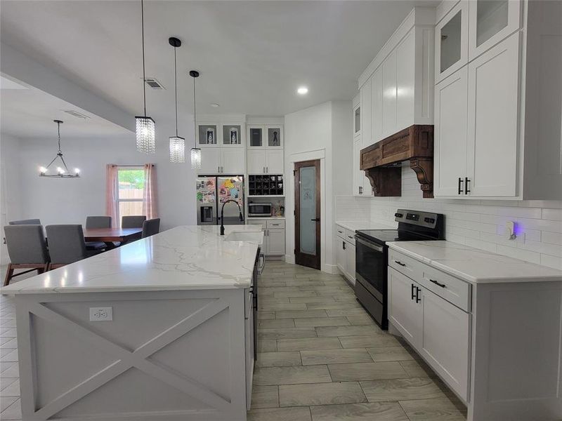 Kitchen featuring glass insert cabinets, stainless steel appliances, white cabinetry, light stone counters, and an island with sink