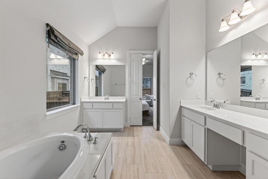 Bathroom featuring two vanities, ensuite bathroom, a bath, and lofted ceiling Bathroom featuring two vanities, ensuite bathroom, a bath, and lofted ceiling