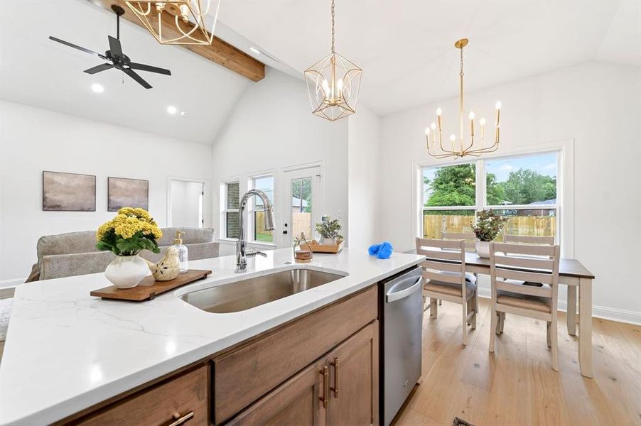 Open-concept kitchen featuring a large island with an undermount sink, a stainless steel dishwasher, wood-finish cabinetry, and light wood-finish flooring