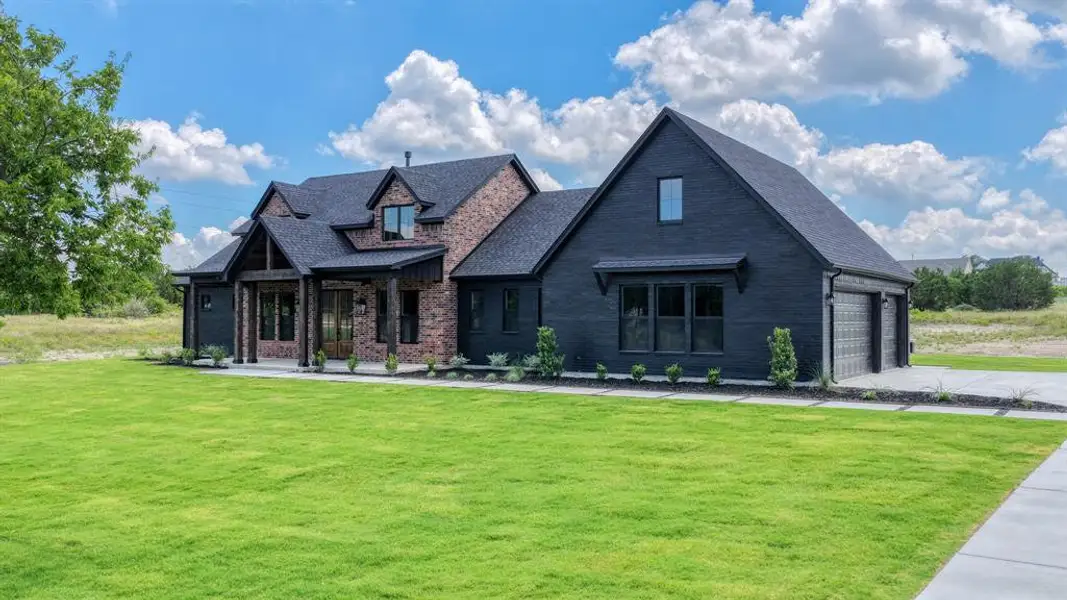 Contemporary exterior featuring dark brick and black siding, a gabled roofline, a covered entry with timber columns, an attached two-car garage, and a concrete driveway