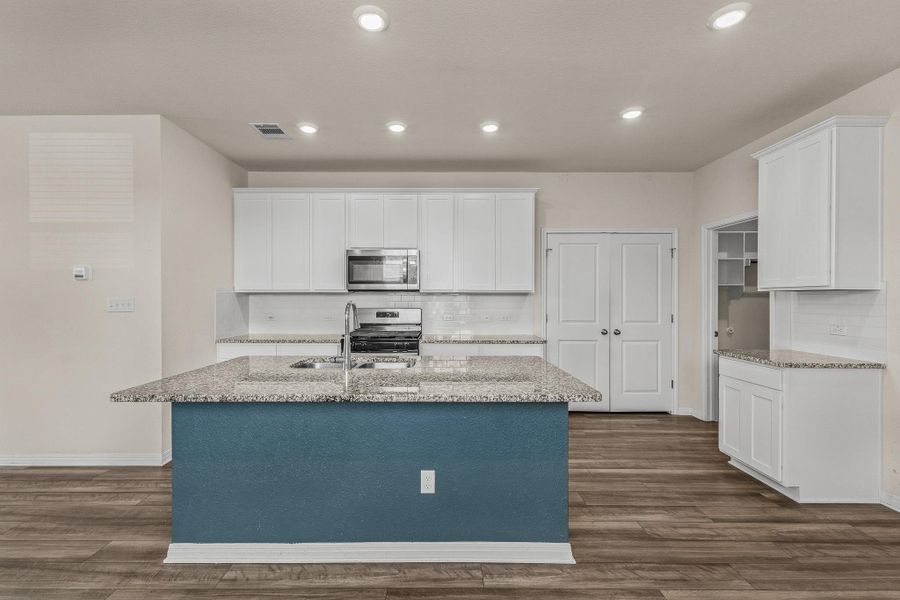 Kitchen with white cabinets, decorative backsplash, light stone counters, an island with sink, and appliances with stainless steel finishes Kitchen with white cabinets, decorative backsplash, light stone counters, an island with sink, and appliances with stainless steel finishes