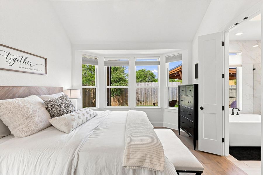 A spacious bedroom features angled ceilings, warm wood flooring, and an elegant bay window.