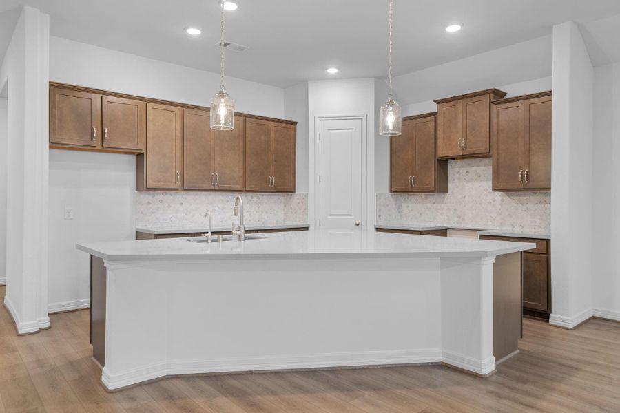 This light and bright kitchen features a large quartz island, white cabinets, a large sink overlooking your family room, recessed lighting, and beautiful backsplash.
