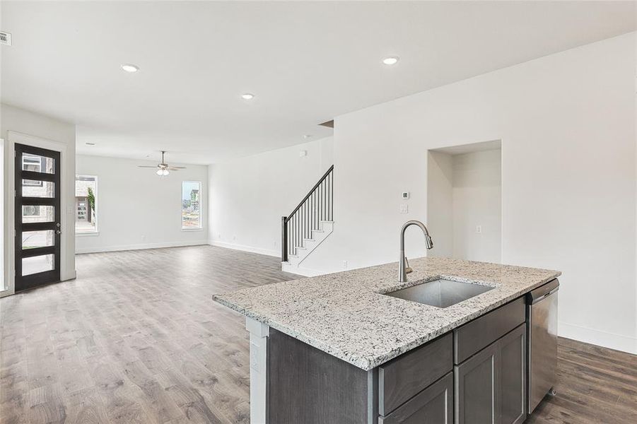 Kitchen with dark brown cabinetry, sink, stainless steel dishwasher, an island with sink, and light stone countertops