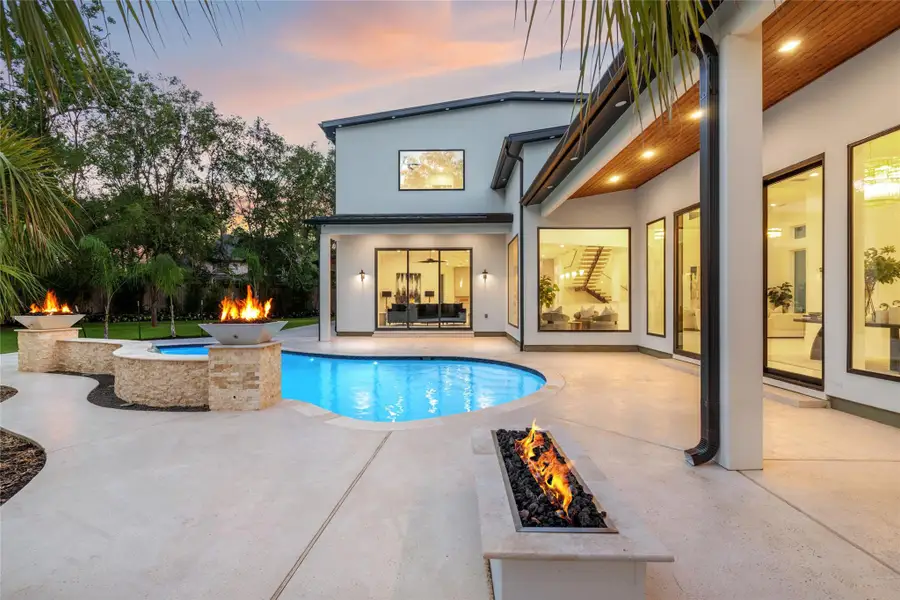 The back of the home is designed for effortless outdoor living, featuring an expansive covered patio with a warm pine-accented ceiling. Just off the primary suite, a sleek linear fire pit offers a private retreat, while the sparkling pool is framed by two dramatic fire bowls The back of the home is designed for effortless outdoor living, featuring an expansive covered patio with a warm pine-accented ceiling. Just off the primary suite, a sleek linear fire pit offers a private retreat, while the sparkling pool is framed by two dramatic fire bowls