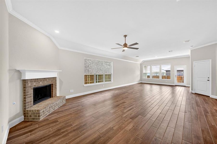 Spacious living area featuring wood-finish plank flooring, a brick fireplace with a white mantel, and extensive window light
