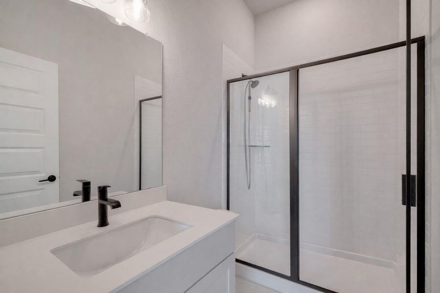 Bathroom featuring a vanity with a white countertop and an integrated sink, a black faucet, and a shower with a black-framed glass enclosure